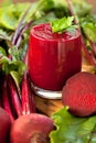 Glass of fresh beetroot juice with bets on wooden table.