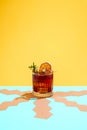 Glass with fresh, delicious Negroni cocktail decorated with slice of dry orange and rosemary over yellow background