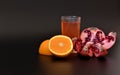 A glass of fresh fruit juice on a black background and pieces of orange and ripe pomegranate nearby Royalty Free Stock Photo