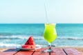 A glass of fresh green tropical fruit juice on the beach, and a plate with watermelon on the table, against the sea. Royalty Free Stock Photo