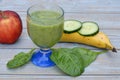 Glass of fresh healthy green smoothie, a red apple, banana, cucumber, and spinach Royalty Free Stock Photo