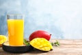 Glass of fresh mango drink and tropical fruits on table against color background. Royalty Free Stock Photo