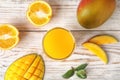 Glass with fresh mango juice and tasty fruits on wooden table