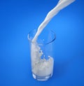 Glass of fresh milk with pouring and splash. On blue Royalty Free Stock Photo