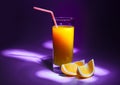 A glass of fresh orange juice with a straw and slices of orange. Violet background and darkening around the edges