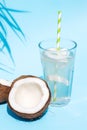 A glass of fresh organic coconut water, milk on a blue pastel background and a ripe half of a coconut next to under palm leaves. Royalty Free Stock Photo