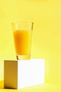 A glass of freshly squeezed refreshing orange juice on a white pedestal or podium. Yellow background. The concept of a healthy Royalty Free Stock Photo