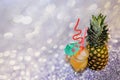 A glass of fruit nectar with ice, decorated with straws and an umbrella next to a ripe pineapple, stands on a gray shiny