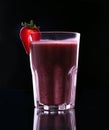 A glass full of juicy, healthy strawberry cocktail on a black background. One-half strawberry with a leaf is on top in a glass cup Royalty Free Stock Photo