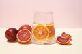 Glass with functional water and slices of citrus fruits and blood oranges on a yellow-pink background, healthy drinks