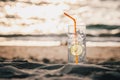 Glass of Gin Tonic with straw and lime slice on the beach, at sunset. Long Beach, Ko Lanta, Thailand.