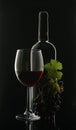 Glass goblet with red wine next to a black glass wine bottle and a bunch of grapes on a black background Royalty Free Stock Photo