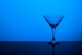 Glass goblet without wine on a thin leg stands on a mirror surface. Back light. Blue background. Copy space Royalty Free Stock Photo