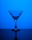 Glass goblet without wine on a thin leg stands on a mirror surface. Back light. Dark blue background. Vertical Royalty Free Stock Photo