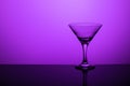 Glass goblet without wine on a thin leg stands on a mirror surface. Back light. Purple background. Copy space Royalty Free Stock Photo