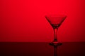 Glass goblet without wine on a thin leg stands on a mirror surface. Back light. Red background. Copy space Royalty Free Stock Photo