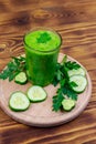 Glass of green detox smoothie of cucumber and parsley on wooden table