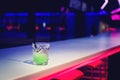 Glass of green neon cocktail in night club lights
