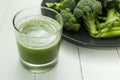 Glass of green smoothie and plate raw broccoli on white wooden background Royalty Free Stock Photo