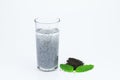 Glass of hairy basil seeds with water and dried seeds on floor with green leaves on white background