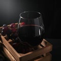 Glass half filled with red wine inside a wooden box with grapes, black background Royalty Free Stock Photo