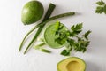 Glass of healthy aloe cocktail with parsley and cut avocado on white table