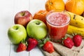 Glass of healthy, fruity juice next to bananas, apples, strawberries, and oranges