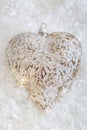 Glass heart on a snow. Blurred white background of glittering bokeh with glowing lights. Christmas decoration. Copy space