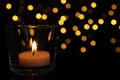 Glass holder with burning tea candle against blurred lights in darkness, closeup. Space for text Royalty Free Stock Photo