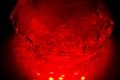 A glass hookah flask filled with bubbling water and smoke glows in the dark in red. luminescence in darkness