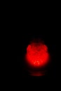 A glass hookah flask filled with bubbling water and smoke glows in the dark in red. luminescence in darkness. vertical