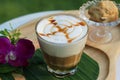 Glass of hot caramel macchiato coffee with cookie and orchid flower on wooden plate in coffee shop of Thailand.