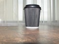 A glass of hot tea in a disposable black covered cup on top of a wooden table