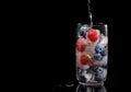 A glass with ice cubes of strawberries and blueberries on a black background with a reflection. Water is poured into a Royalty Free Stock Photo