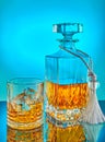 Glass and square crystal decanter with scotch whiskey or brandy on a blue gradient background with reflection Royalty Free Stock Photo