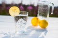 Glass of ice and water decorated with a slice of lemon standing on a white table against a decanter with water and two Royalty Free Stock Photo