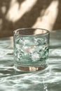 A glass of ice and water on a rippling surface is illuminated by sunlight, casting beautiful caustics and leaf shadows on a Royalty Free Stock Photo