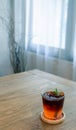 Glass of iced black tea with lemon decorated with rosemary on a wooden table