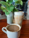 a glass of iced coffee milk, a cup of hot coffe milk, and a pot contains plants with fresh green leaves Royalty Free Stock Photo