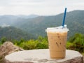 A glass of iced coffee is placed on a rock against a background of mountains and sky