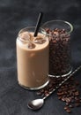 Glass of iced cold coffee and milk with free raw coffee beans in glass container with long spoon on black Royalty Free Stock Photo