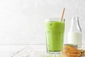 Glass of iced green matcha latte with a straw and bottle of milk on white tile background Royalty Free Stock Photo