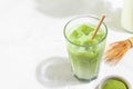 Glass of iced green matcha latte with a straw and bottle of milk on white tile background with hard shadows Royalty Free Stock Photo