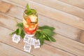 A glass of iced lemon mixed fruit tea with fresh mint leaves and ice cubes scattered on the table