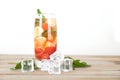 A glass of iced lemon mixed fruit tea with fresh mint leaves and ice cubes scattered on the table