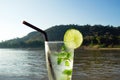 A glass of iced mojito with lime and leaves of mint on a background of river during of sunset.