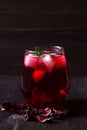Glass of iced red hibiscus tea and dry flowers on a wooden table. Royalty Free Stock Photo