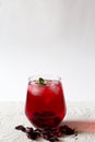 Glass of iced red hibiscus tea with dry rose flowers on a white table. Royalty Free Stock Photo