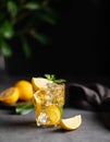 A glass of iced tea with lemon and mint on a dark background with citrus fruits and branch