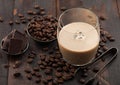 Glass of Irish cream baileys liqueur with ice cubes, coffee beans and dark chocolate in steel bowl on dark wood background Royalty Free Stock Photo